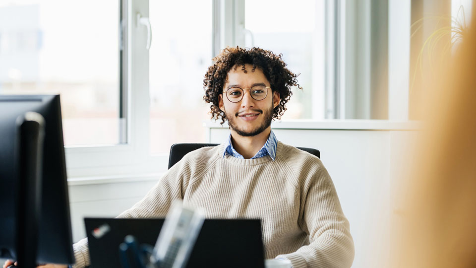 Employee with glasses and curly hair works at a computer.