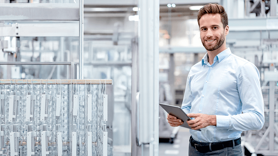 Man in shirt standing in a factory holding a tablet in his hand