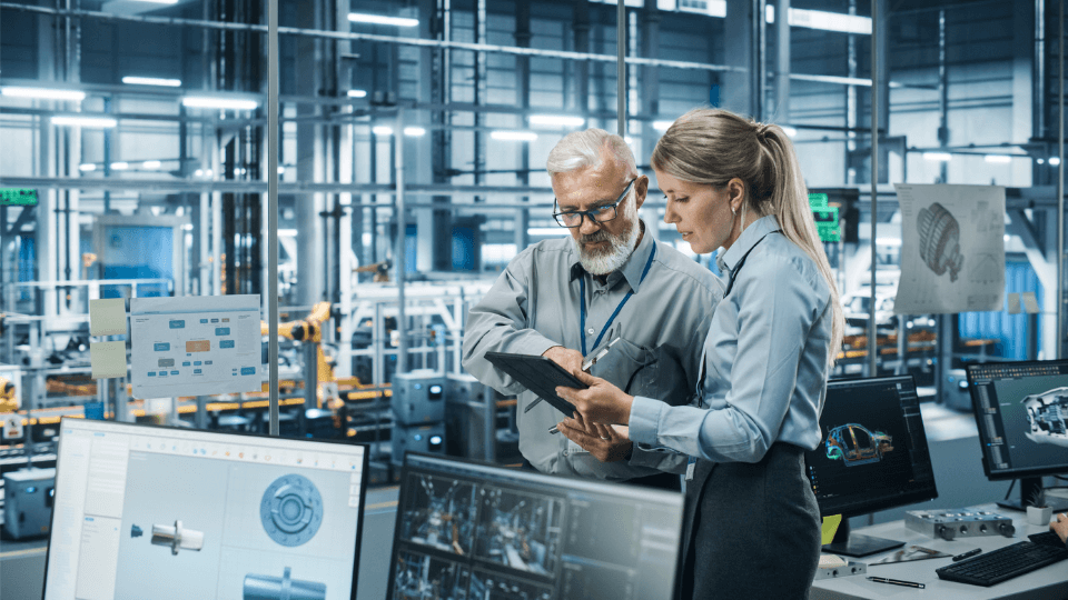 Two people standing in an office in an industrial factory environment looking at a tablet